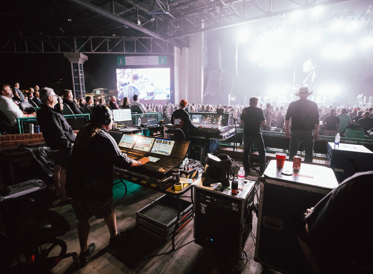 View of front of house sound and lighting technicians with crowd and stage